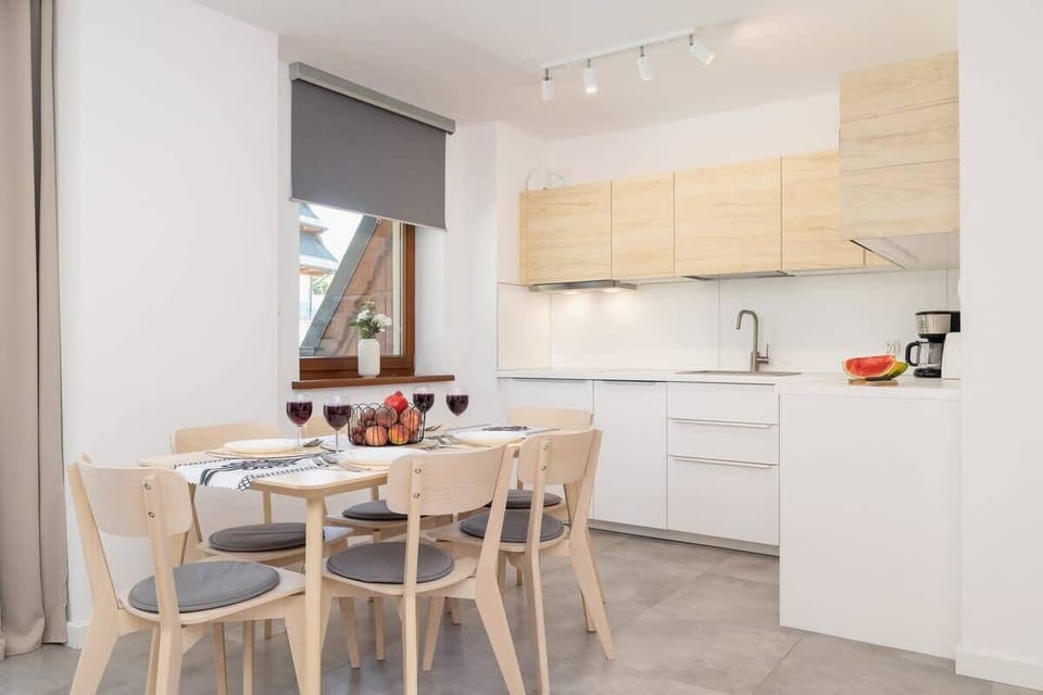 A modern kitchen with wooden cabinets, white countertops, and a dining area with a round table and chairs, blending functionality and style.

