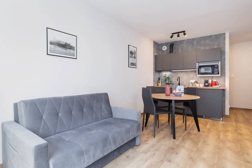 A wide view of the living and dining area, featuring a gray sofa, a dining table, and a functional kitchen, all in a cohesive and bright design.
