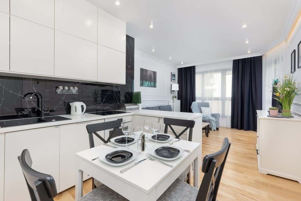A dining area with a white table and black chairs, set with plates and glasses, blending elegance and functionality.
