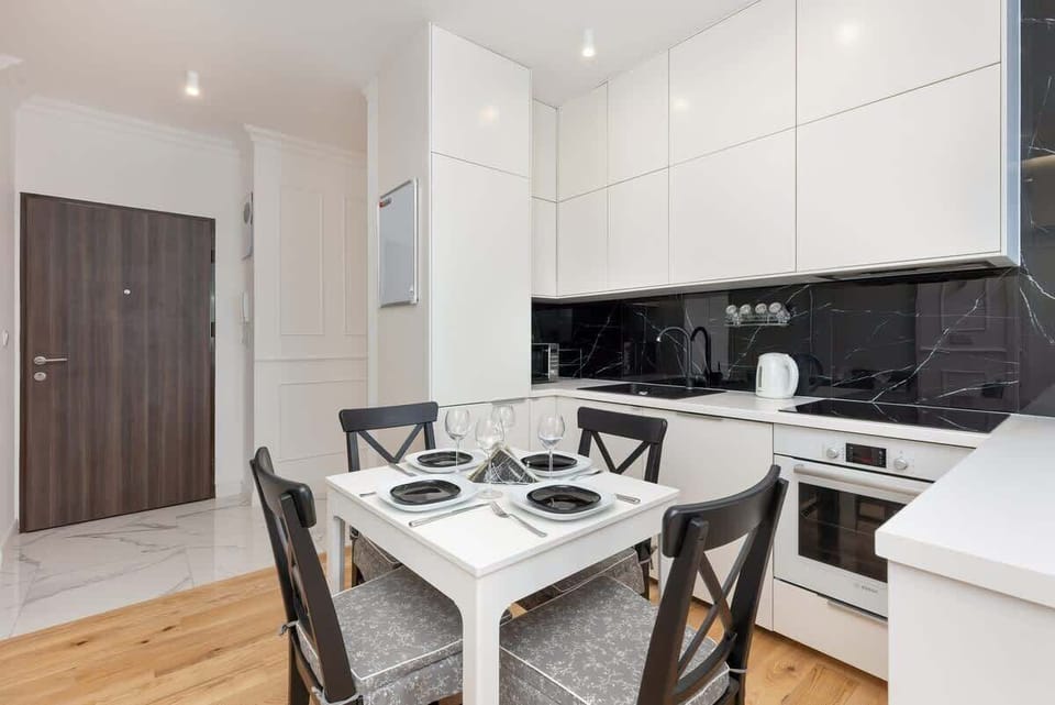 A compact yet functional kitchen with white cabinets and black countertops, adjacent to a small dining table set for two.

