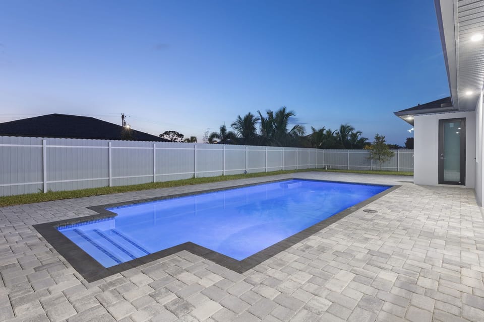 Pool lit up at night with the fenced backyard