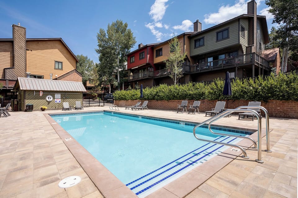 A sparkling outdoor pool invites relaxation beneath blue skies, surrounded by comfortable loungers and lush greenery. Your ideal mountain retreat awaits.