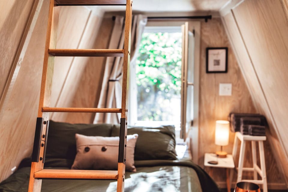 Climb into cabin comfort with a queen bed below, loft ladder above, and soft light for restful nights