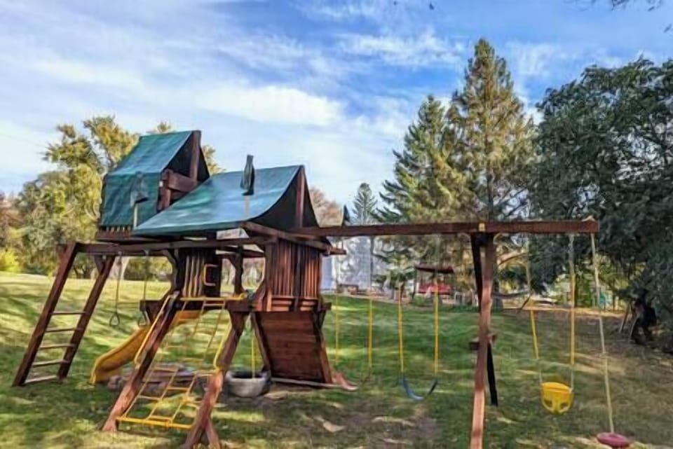 The playset has a tire swing, monkey bars, climbing wall, multiple swings, fort, slide & sandbox.