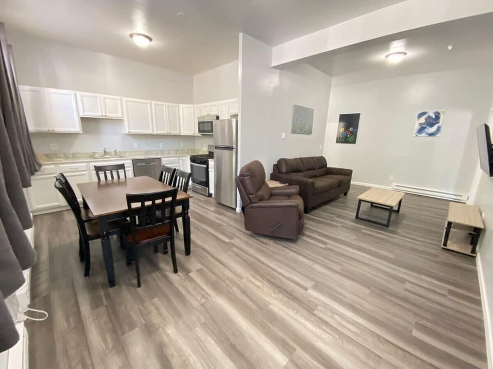 A spacious open floor plan connects the kitchen, dining, and living areas. The kitchen has modern appliances, the dining area features a sleek table and chairs, and the living room offers a plush sofa with natural light streaming through large window