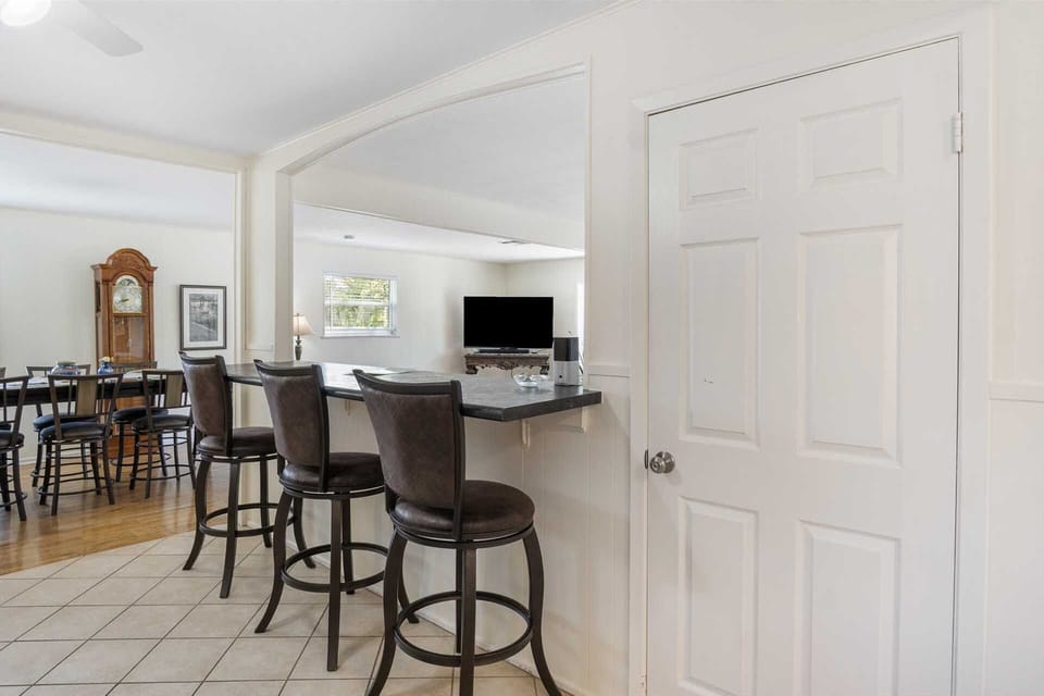 This functional kitchen pass-through features a breakfast bar with stylish high-back stools, offering a clear view into the bright dining and living areas.