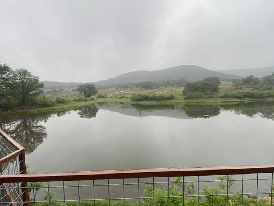 A peaceful, misty morning by the lakeside, where calm waters mirror the rolling hills and quiet countryside.