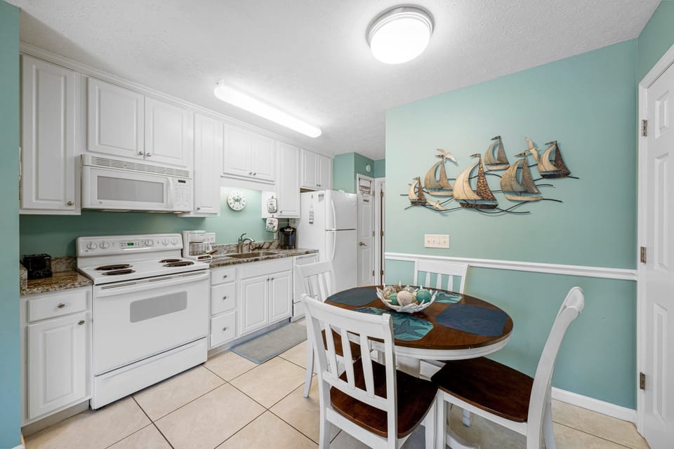 Cheerful kitchen & dining area w/ white cabinets, full appliances & a cozy table for meals.