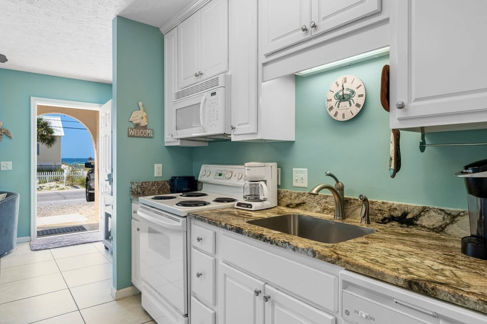 Compact kitchen w/ white cabinetry, dark countertops & everything you need to cook up a meal.