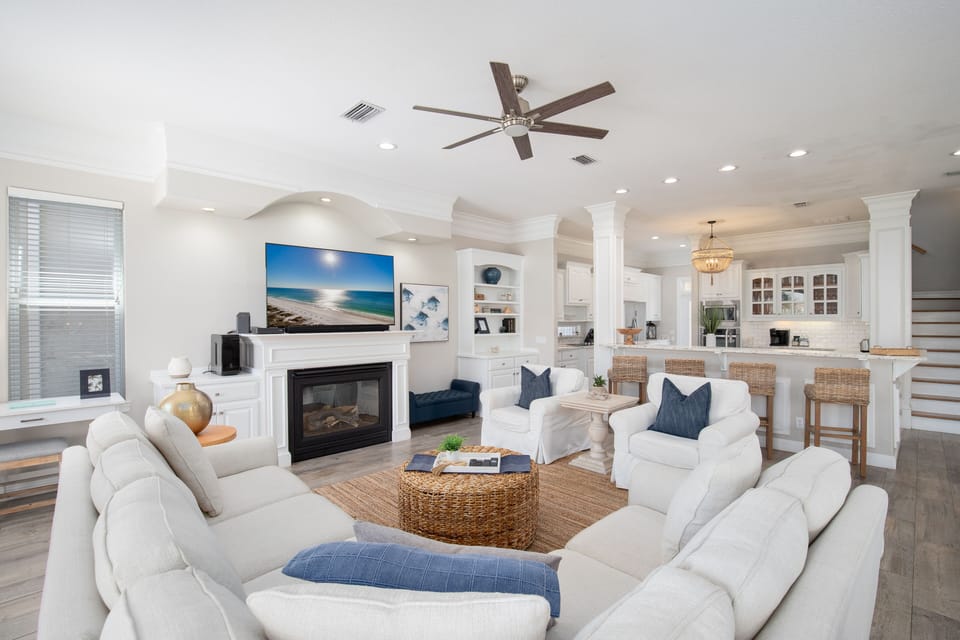 Sink into plush white sofas in your open-concept living space, where coastal blues meet warm wicker accents and your fireplace creates the perfect gathering spot.