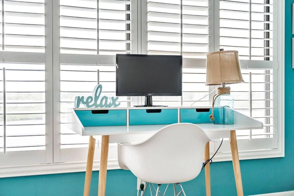 Sunny workspace nook w/ a desk, chair, & shutters letting in soft natural light.