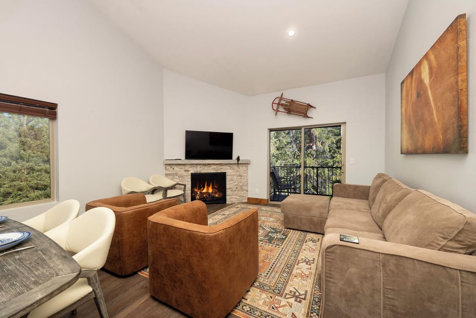 Sink into plush seating by your crackling fireplace, where forest views and cozy warmth create the perfect retreat.