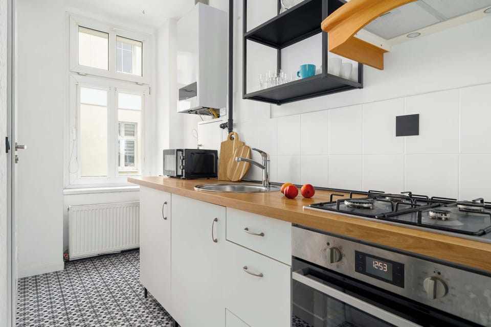 A narrow kitchen includes white cabinets, a stove, and wooden countertops extending along the wall. Open shelving adds practical storage.