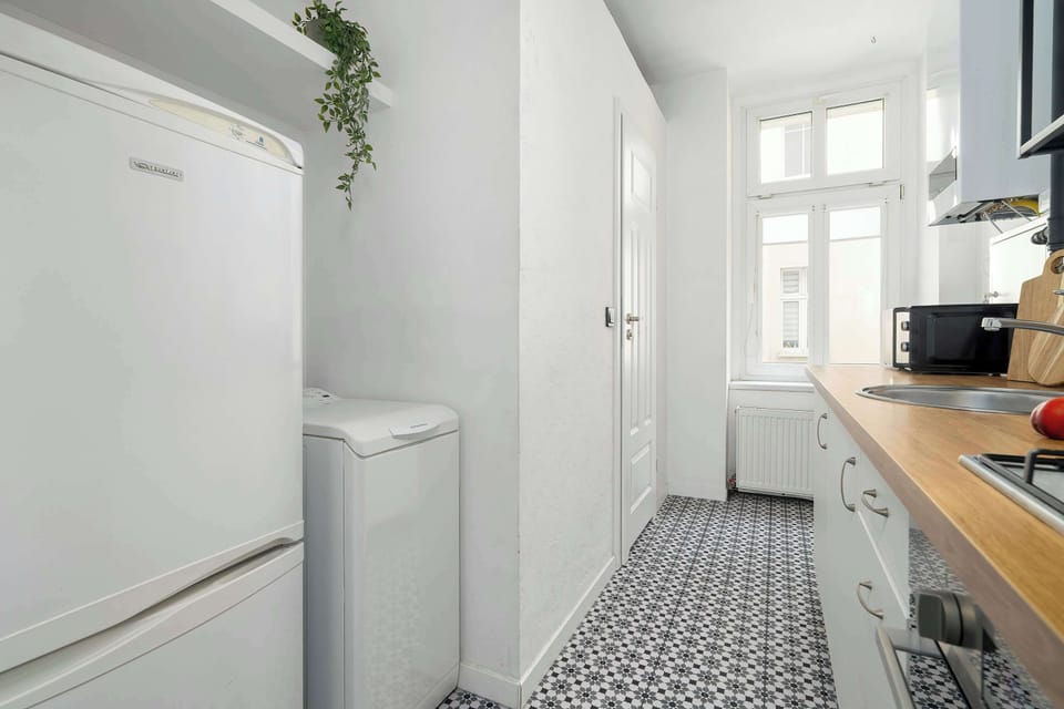 A galley-style kitchen stretches toward a refrigerator at the far end of the room. Patterned flooring adds visual texture.