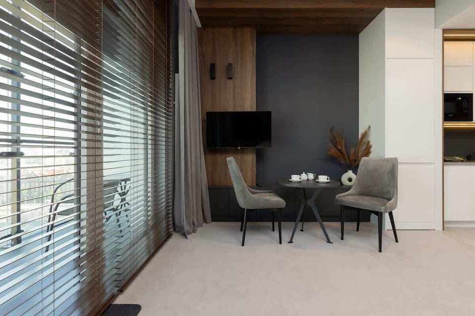 A cozy dining area near floor-to-ceiling windows, with a small table and chairs, ideal for enjoying natural light.
