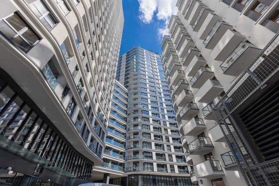 A tall view of the modern apartment complex with glass facades and intricate architectural details, set against a bright sky.
