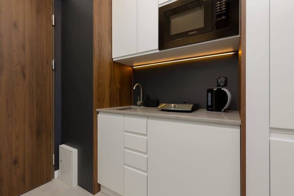 A kitchenette with white cabinets, a wooden accent wall, and sleek black appliances, blending functionality with minimalism.

