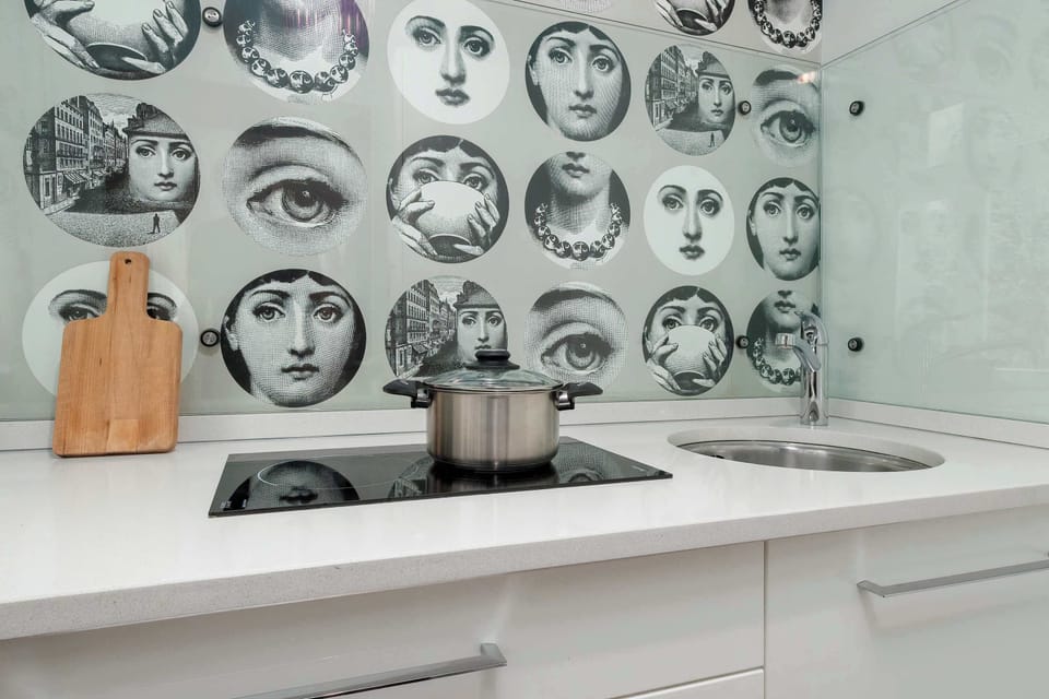 A close-up of a stylish kitchen backsplash with artistic face illustrations. The countertop is tidy and organized, adding character to the space.
