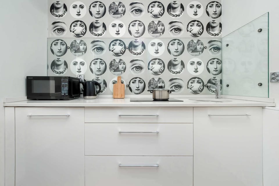 A modern white kitchen counter with cabinets and patterned wall décor. The design feels sleek and functional with plenty of storage space.