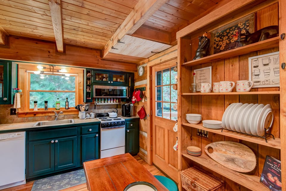 Charming log cabin kitchen at Casa Haven with teal cabinetry, open shelving stocked with dishware, and a warm wood ceiling overhead.