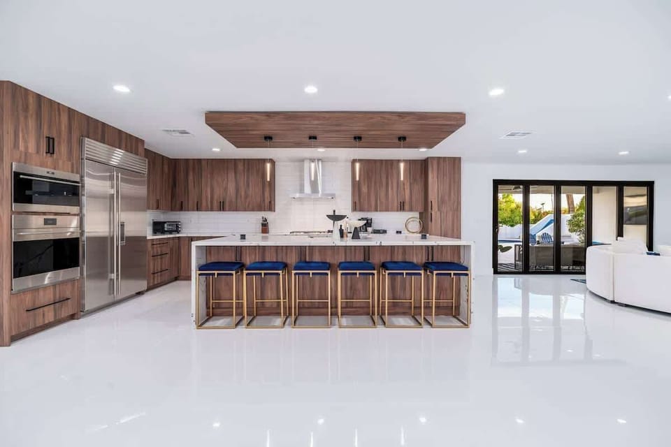 Step into your dream kitchen with rich walnut cabinetry and gleaming marble countertops, where six stylish barstools invite memorable meals and conversations by the pool.