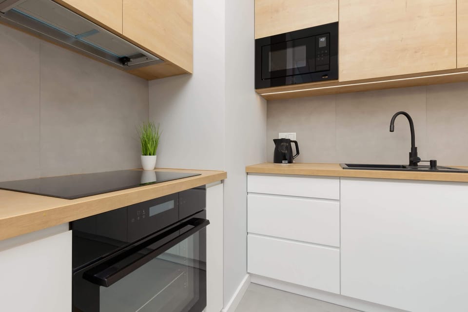 A sleek kitchen with white cabinets, wooden countertops, and black appliances, blending functionality and modern aesthetics.
