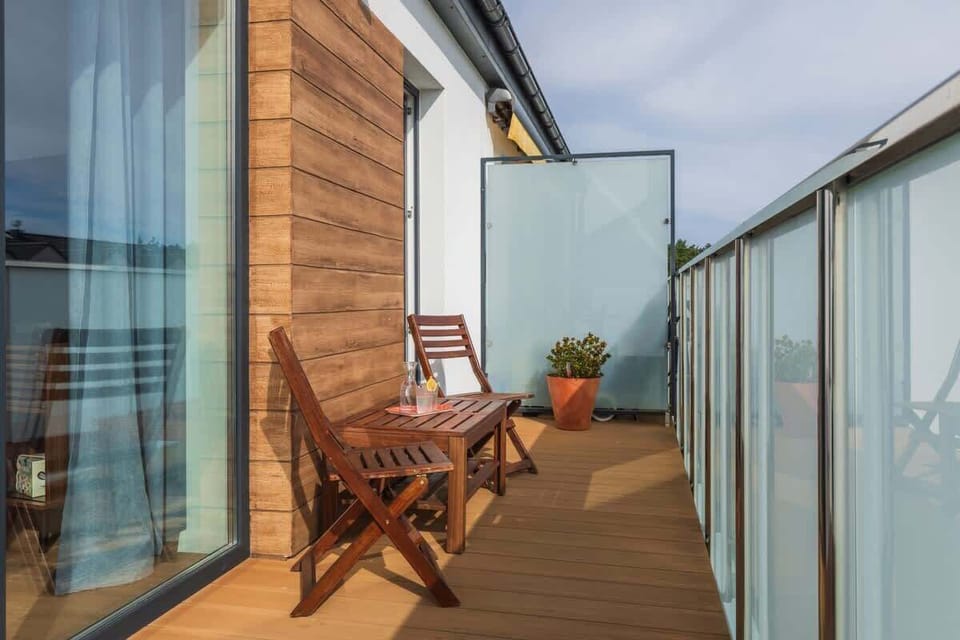 A balcony with wooden flooring, small seating, and potted plants, offering a cozy outdoor space with a view.

