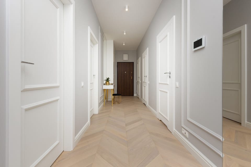 A bright hallway with white walls, light wooden flooring, and sleek panel doors leading to different rooms.

