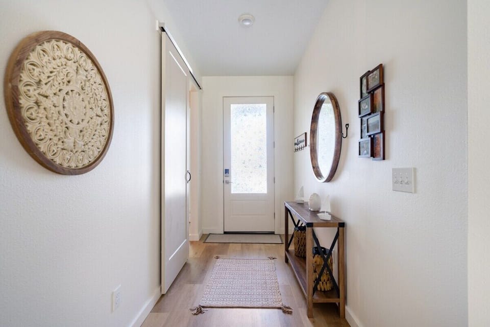 FRONT DOOR EXIT: As you walk through our hallway, elegant Scandinavian design adorns the walls. To the right, the foyer exudes its own Scandinavian charm with a round mirror and framed wall art, showcasing our great interiors