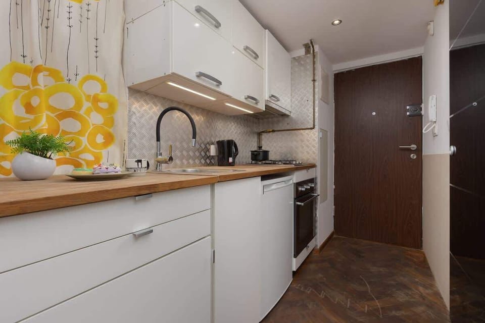A bright kitchen shot featuring a cheerful yellow-and-white backsplash, white cabinetry, and a stainless-steel sink.

