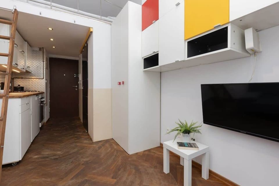 A hallway perspective showing the loft ladder, high ceiling, and continuous parquet floors.

