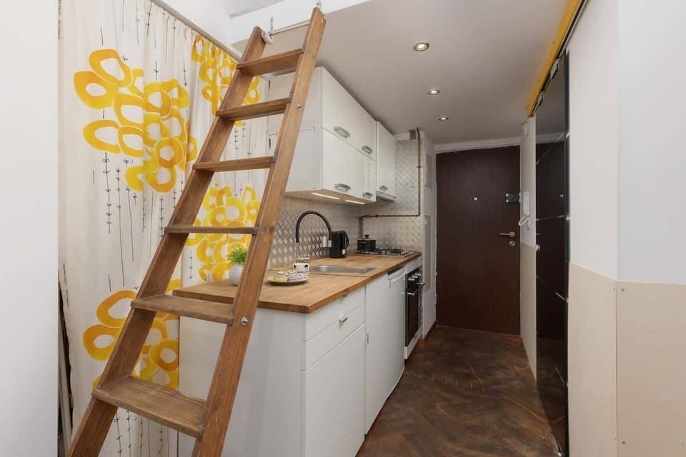 A view of the loft ladder and a compact kitchenette on warm parquet flooring, offering a functional, open-plan layout.

