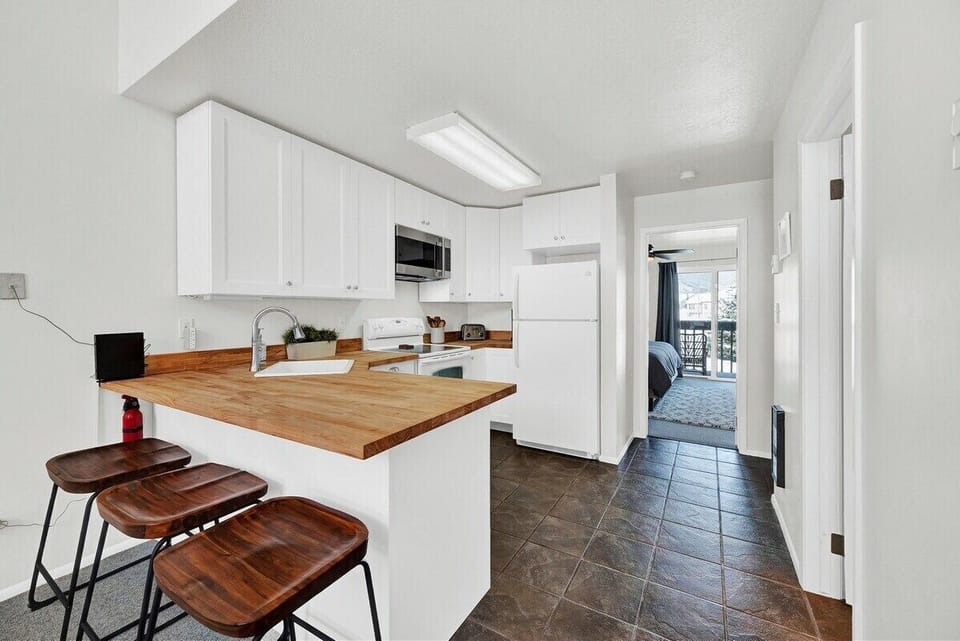 Functional kitchen with white cabinetry, wood countertops, bar seating, and easy flow into the nearby bedroom and living areas.