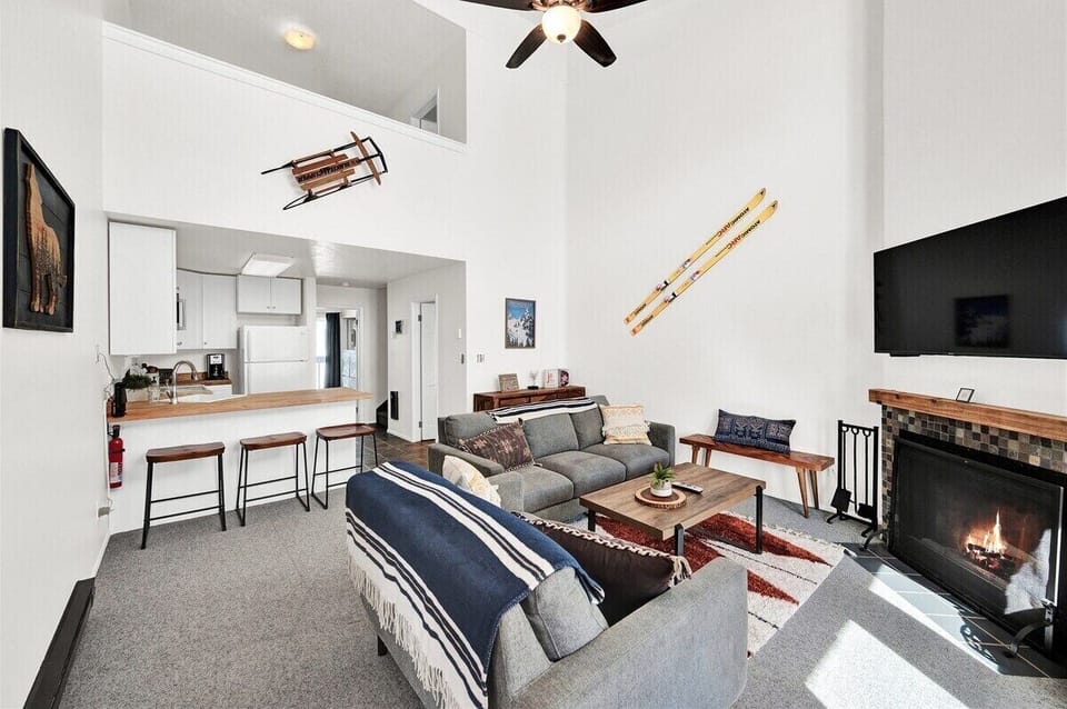 Bright open-concept living space with a cozy fireplace, comfortable seating, ski-themed décor, and convenient access to the kitchen.