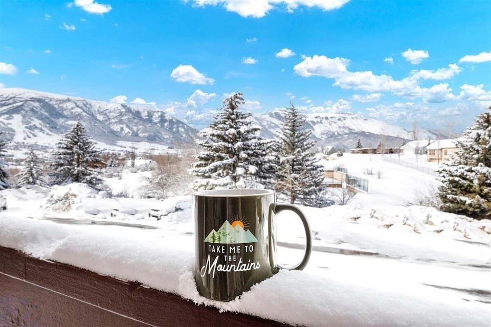 A cozy balcony moment featuring a mountain-themed coffee mug set against a beautiful snowy Ogden Valley backdrop.