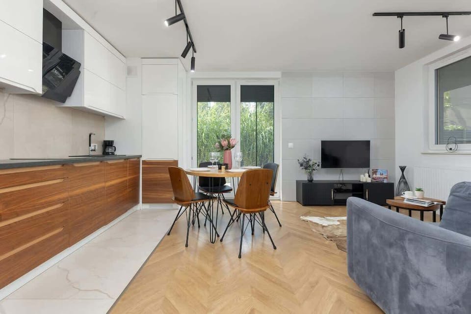 A modern open-plan dining and living area featuring wooden floors, a stylish wooden dining table, and a cozy gray couch.