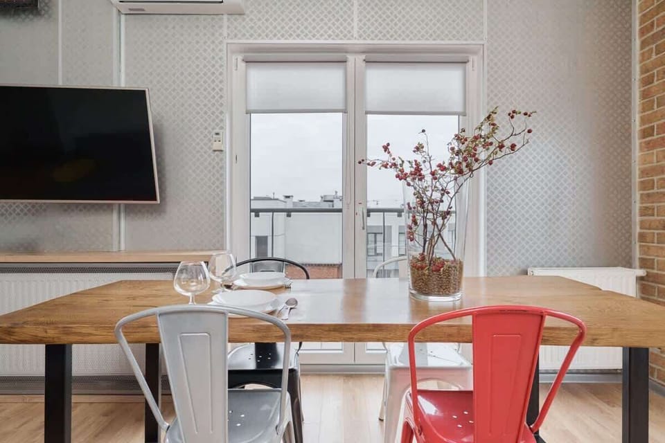 A dining space with a table set with flowers, a mix of industrial and modern decor, and a view of the living room.







