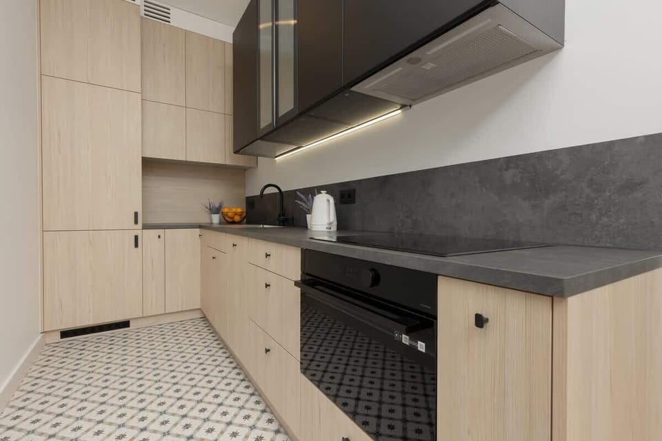 A modern kitchen with wooden cabinets, patterned floor tiles, and built-in appliances.
