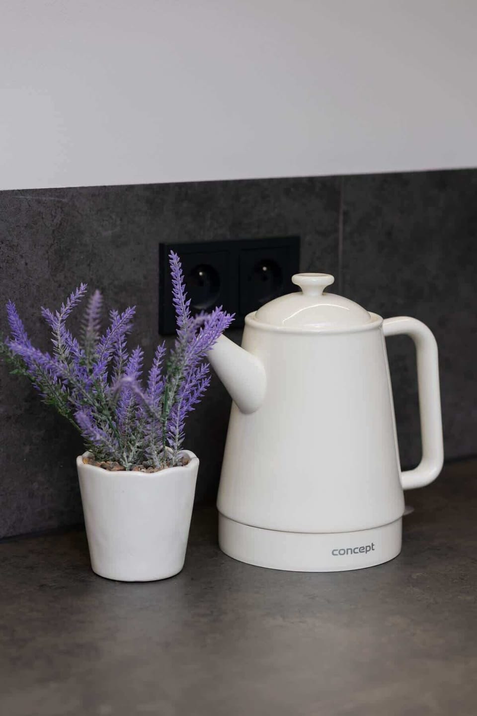 A close-up of lavender flowers and a white electric kettle on a kitchen counter.
