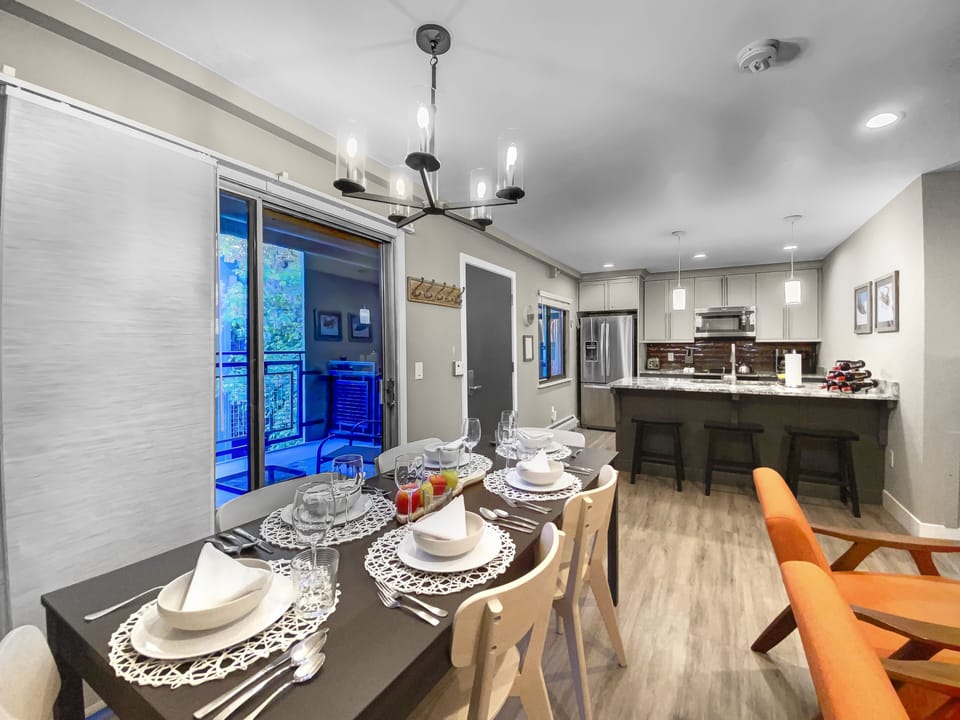 Bright, modern dining and kitchen area featuring a fully set table, sleek appliances, and warm lighting. Perfect for family meals and après-ski gatherings, offering a stylish and comfortable space for your Park City vacation rental stay.