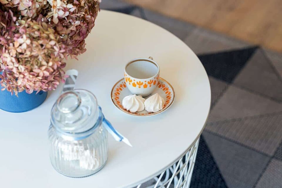 A close-up of a small table set with a jar candle, two cups, and dried flowers beside a white cushion.