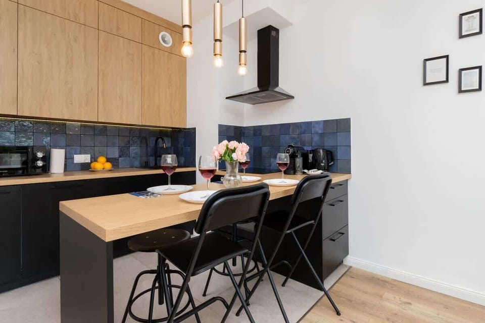 A modern kitchen with light wood cabinets, black backsplash, and a small dining table with black chairs.