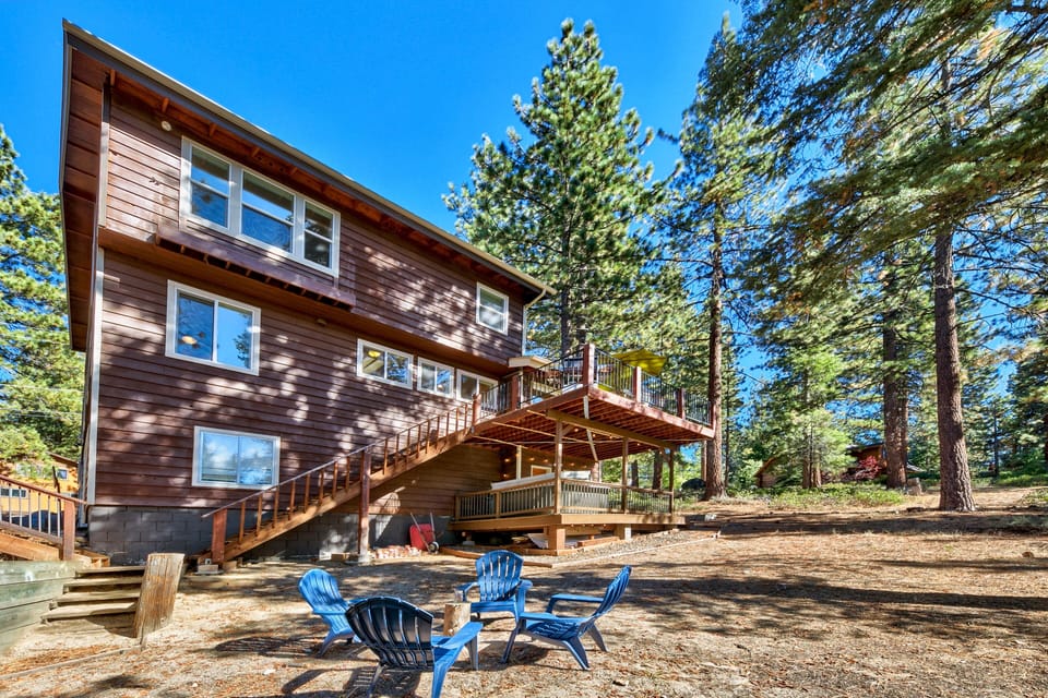Modern mountain cabin with multi-level decks nestled among towering pines under brilliant blue skies.