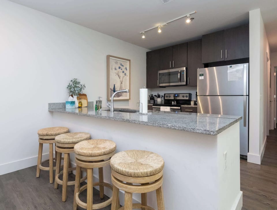 A functional breakfast bar with three woven stools, providing a casual transition into the modern kitchen area.