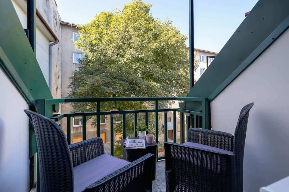 A compact balcony with two chairs and a table, surrounded by a railing and trees in the background.