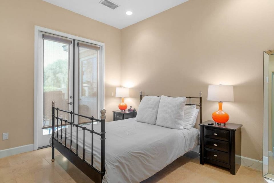 Orange accent lamps—metal bed frame and sliding door access to backyard pool.