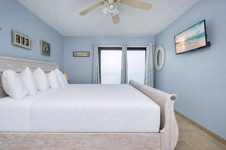 The master bedroom features a cozy white bed, a wall-mounted TV, and serene blue walls, creating a relaxing retreat
