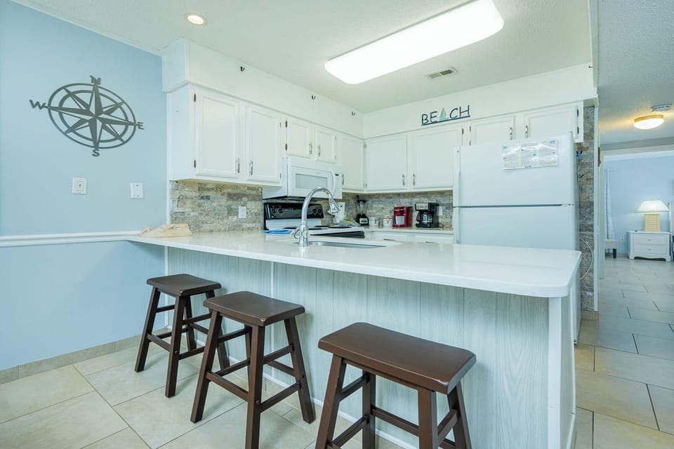 This kitchen features white cabinetry, stainless appliances, and a stylish bar area with wooden stools for casual dining