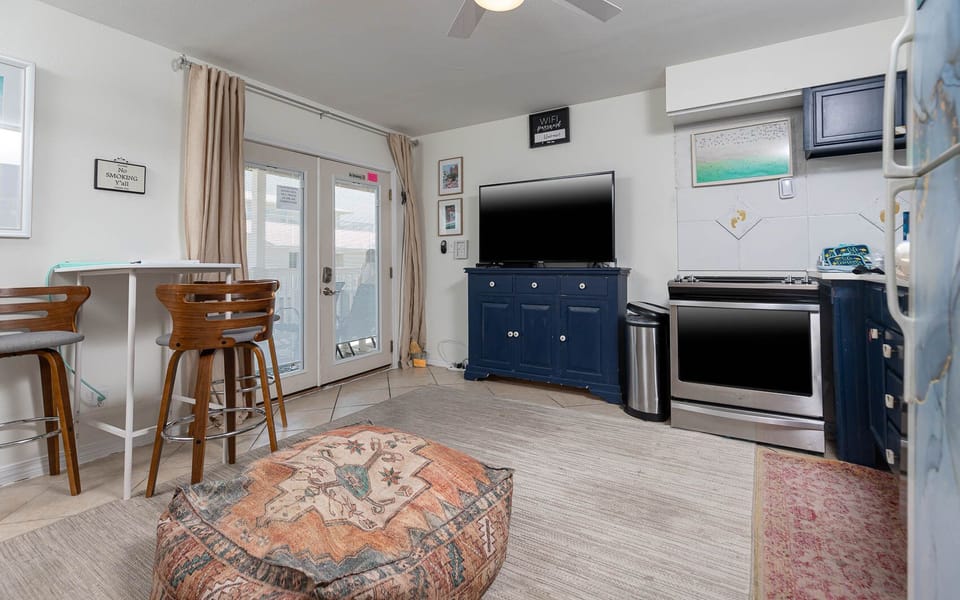 The living area features a large TV, stylish blue cabinetry, and a comfortable seating area leading to a lovely outdoor view