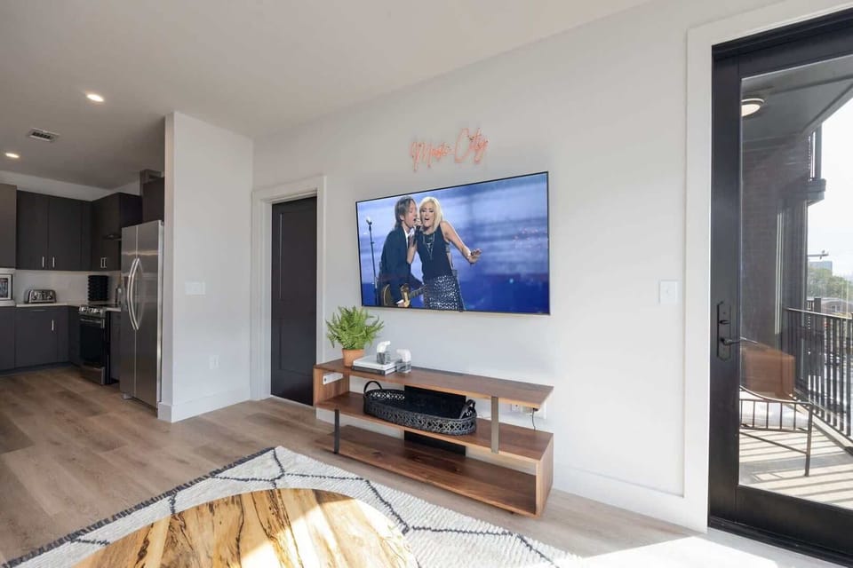 Modern open concept living area with floor to ceiling windows, designer furniture, smart TV, and access to private patio.
